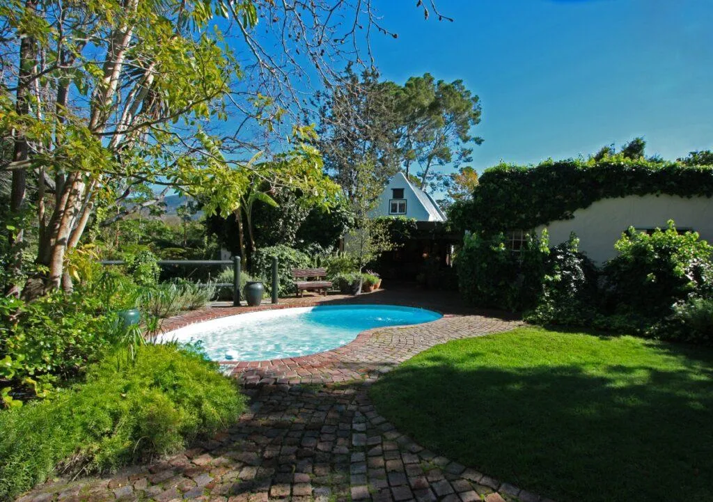 Small pool in a lush garden with a white house in the background