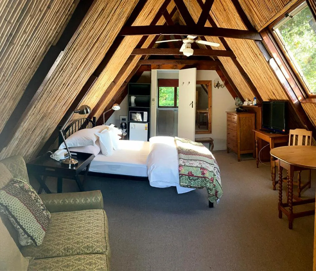 Cozy attic bedroom with wooden beams bed sofa and ceiling fan
