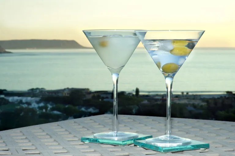 Two martinis with olives on a table overlooking the ocean at sunset
