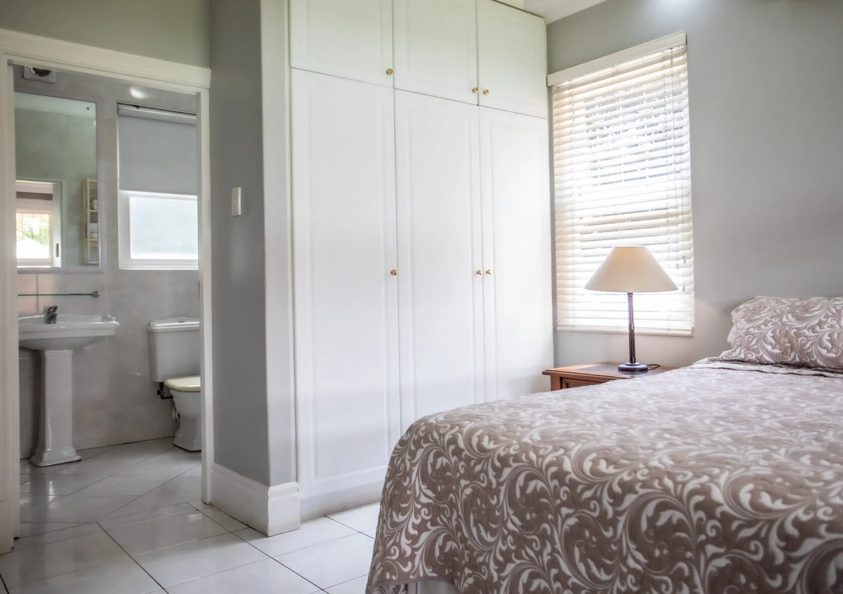 Bedroom with patterned bed white wardrobe and adjacent bathroom visible through doorway