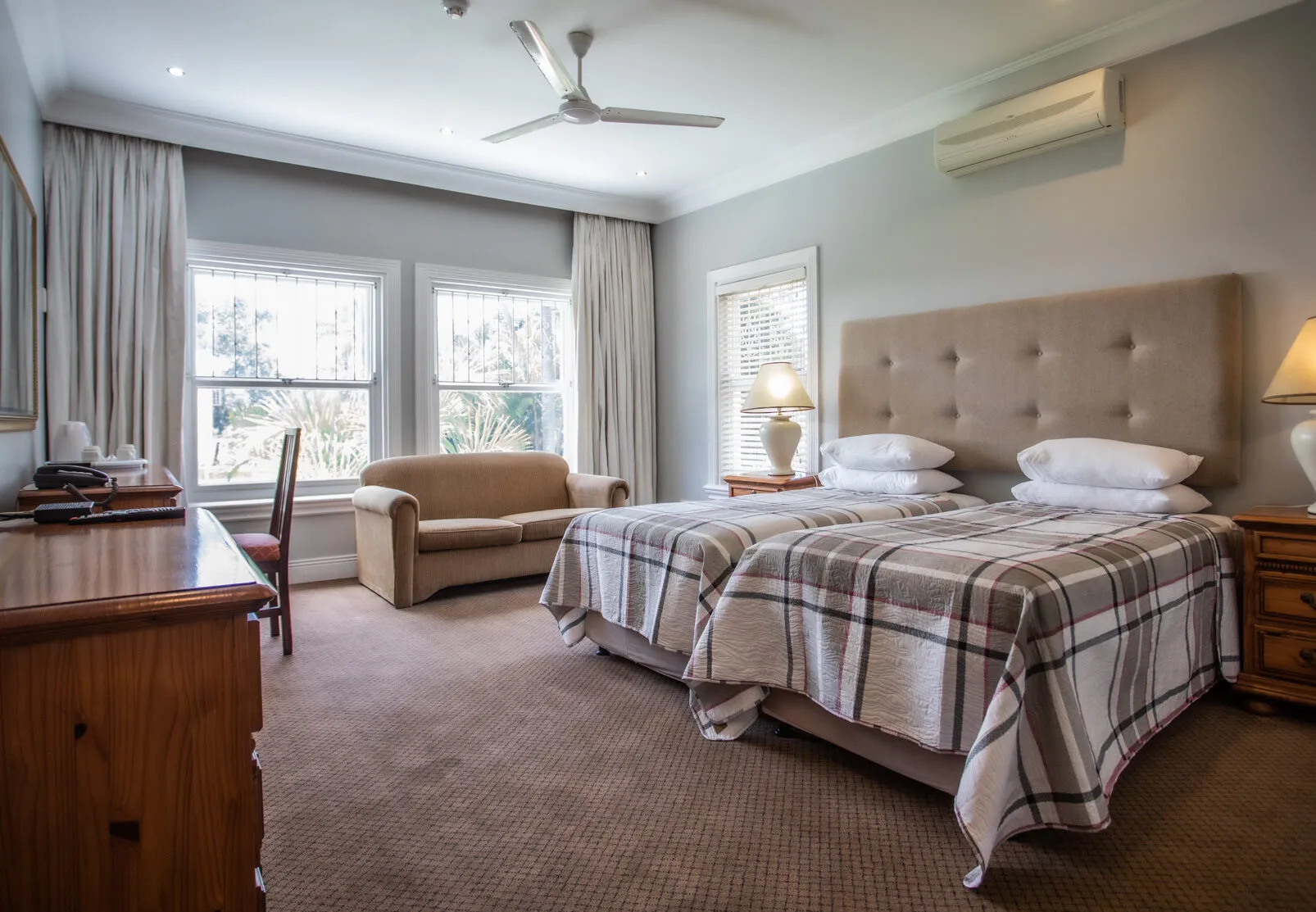 Bedroom with two single beds sofa desk and large windows with curtains