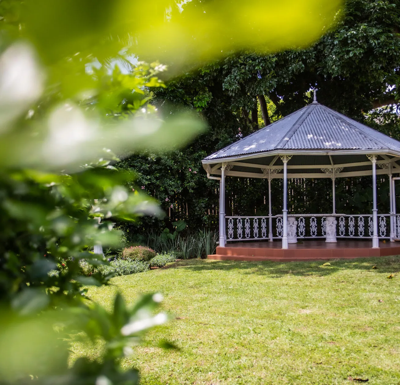 Gazebo in a lush green garden with blurred foliage in the foreground