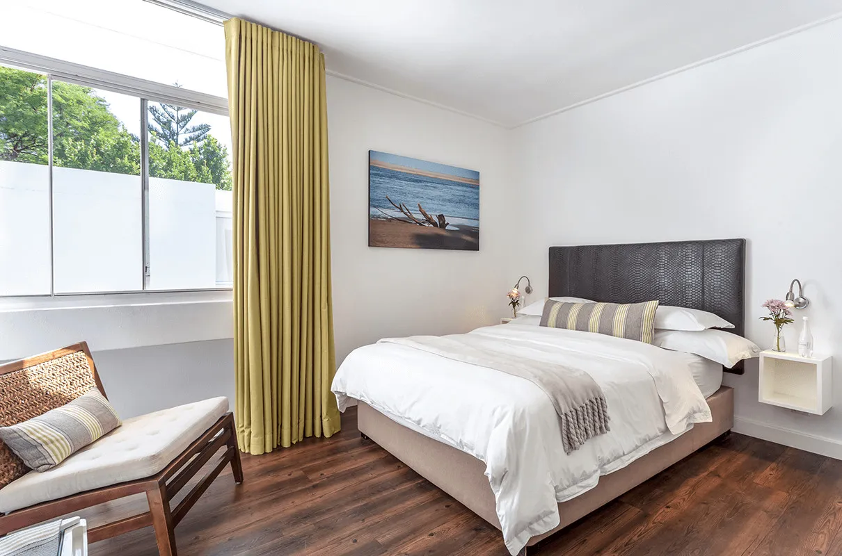 Cozy bedroom with a large bed wooden floor and yellow curtains