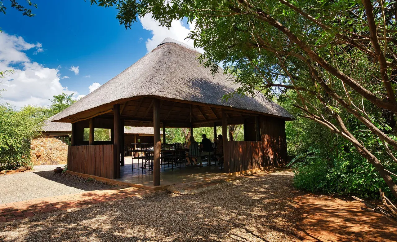 Wooden gazebo with thatched roof in a lush green outdoor setting