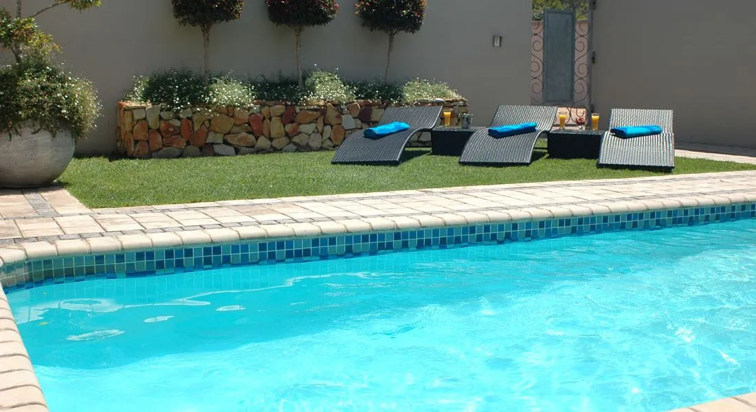 Swimming pool with lounge chairs potted plants and stone wall in a backyard
