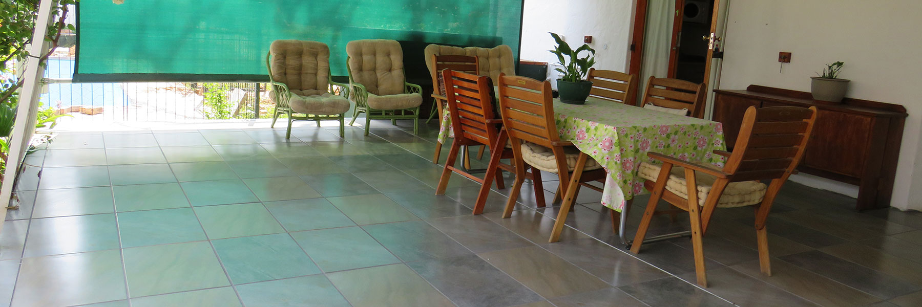 Dining area with wooden chairs and table, covered patio, green mesh screen.