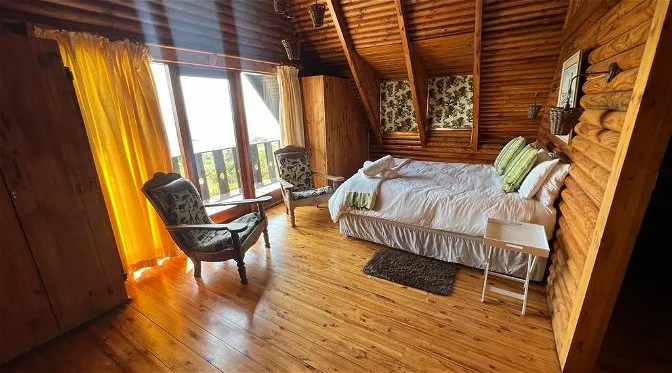 Cozy wooden cabin bedroom with large windows bed and armchairs
