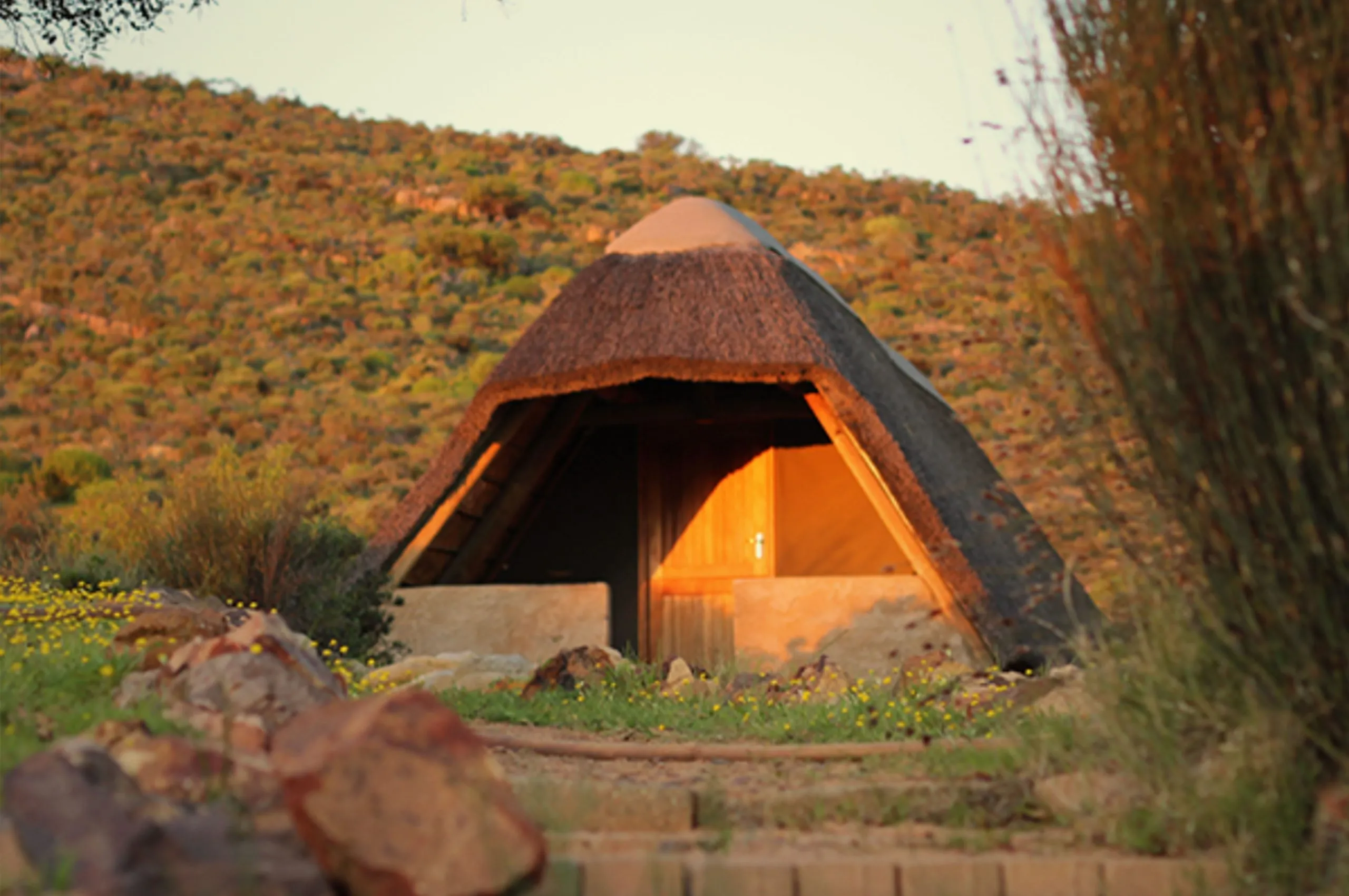 A thatched hut in a hilly grassy landscape during sunset
