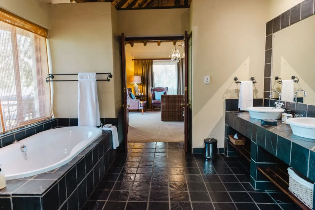 Modern bathroom with bathtub dual sinks and view into a bedroom