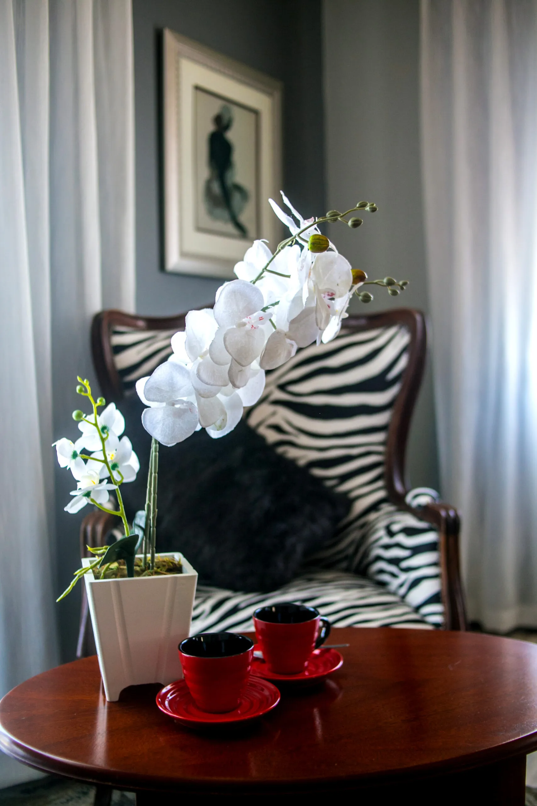 White orchids on a table with red cups and a zebrapatterned chair