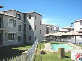 Apartment complex with a swimming pool and grassy area under a blue sky