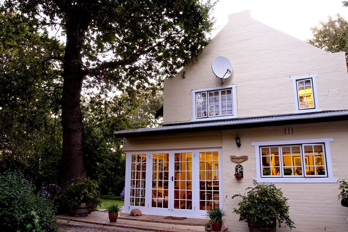 House with large windows and satellite dish surrounded by trees and plants