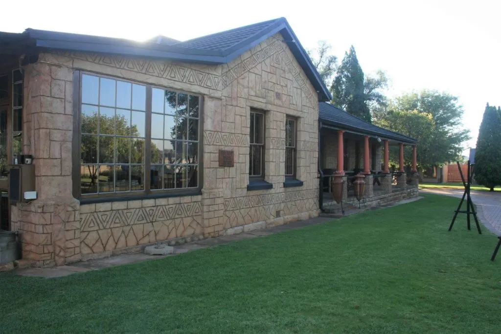 Stone building with large windows and a covered veranda surrounded by grass and trees