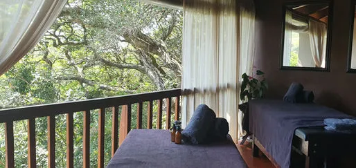 Two massage tables on a wooden deck with forest view and draped curtains