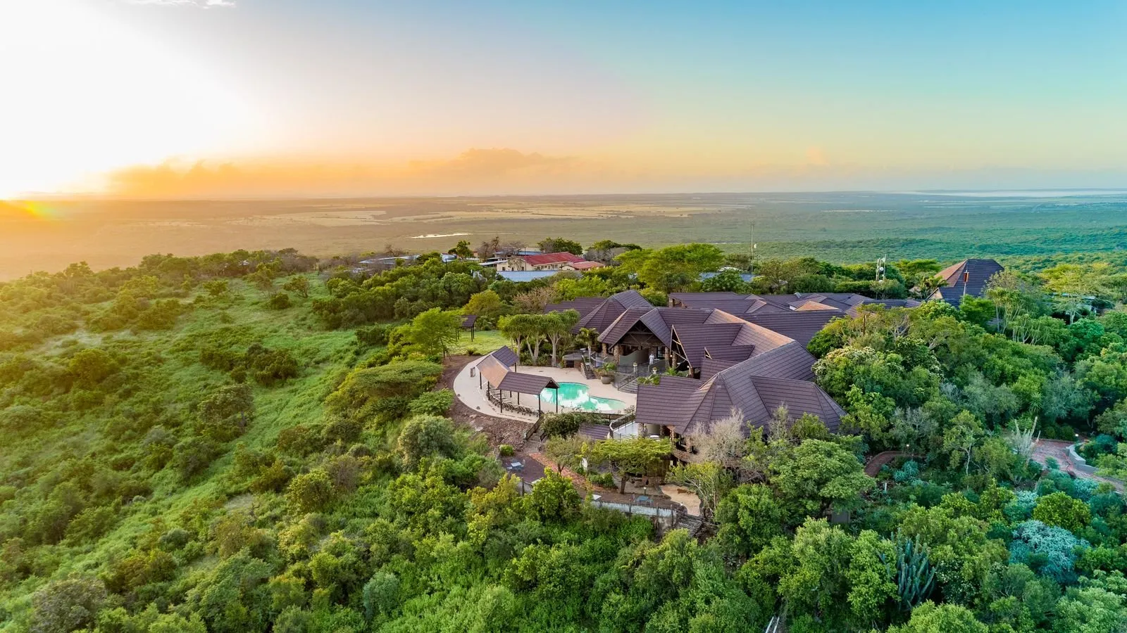 Aerial view of a large house surrounded by lush greenery at sunset