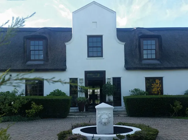 White building with black windows thatched roof and a lion fountain in front