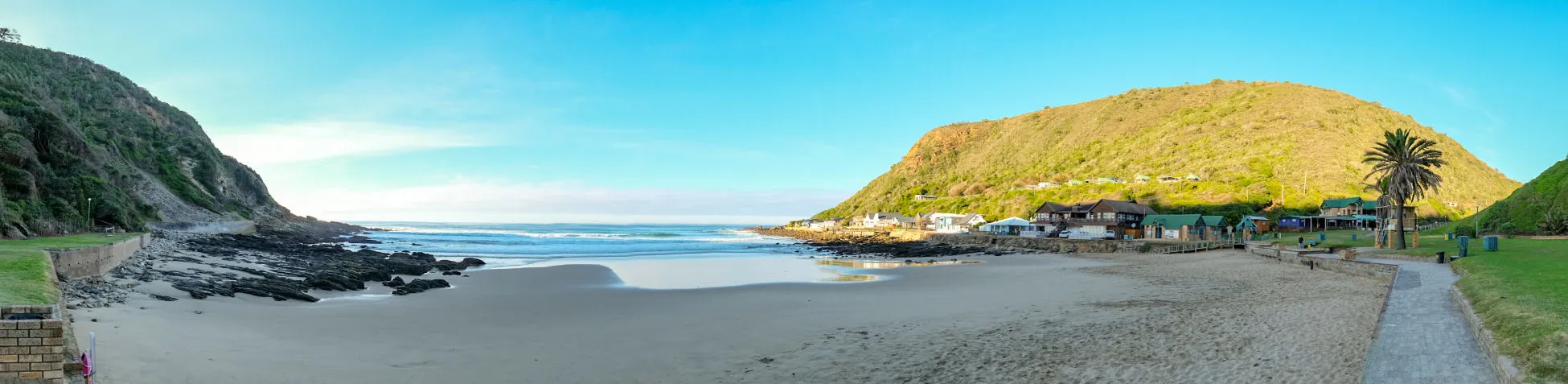 Panoramic view of a beach with green hills and a clear blue sky