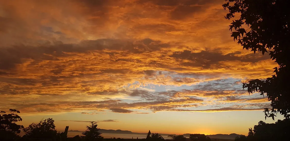 Sunset with vibrant orange and yellow clouds over a distant landscape with trees