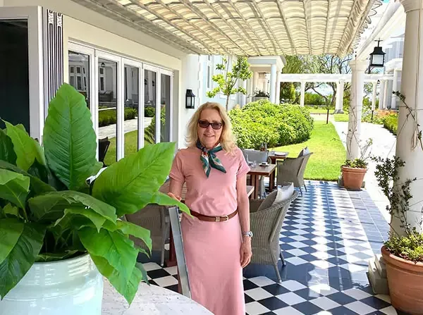 Woman in pink dress standing on a checkered patio with plants and furniture