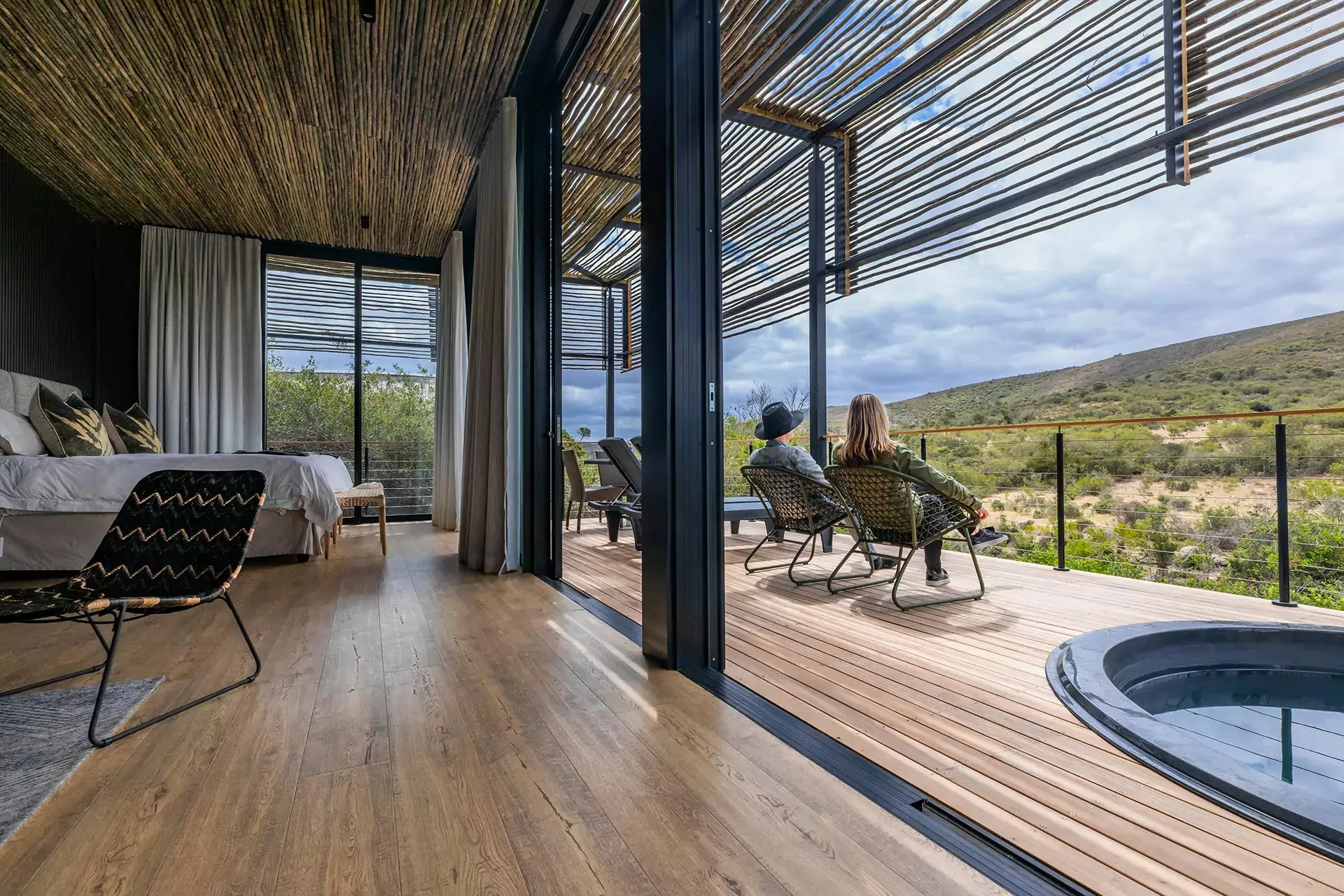 Modern room with large windows two people sitting outside overlooking a scenic landscape