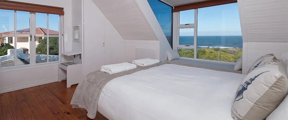 Bright bedroom with large windows overlooking the ocean wooden floor and white bedding
