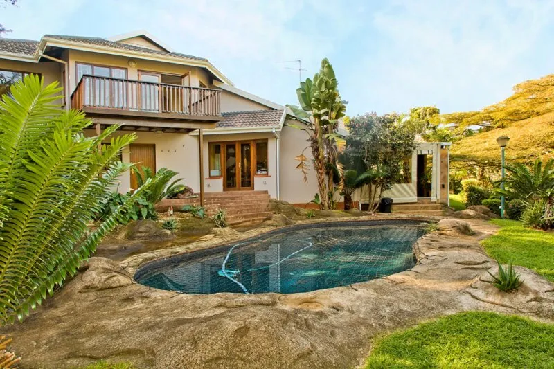 Twostory house with a backyard pool surrounded by greenery and rocks
