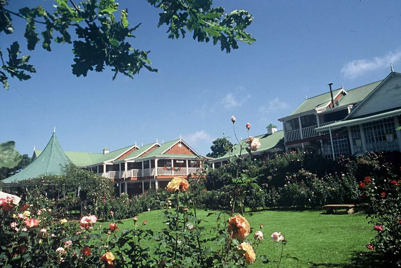 Large house with green roof surrounded by blooming roses and trees
