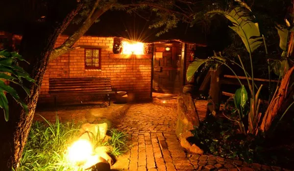 Warmly lit brick building with pathway bench and surrounding plants at night