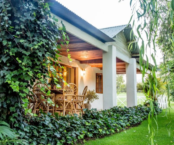 Cottage with a veranda, wicker furniture, and lush greenery in a garden setting.