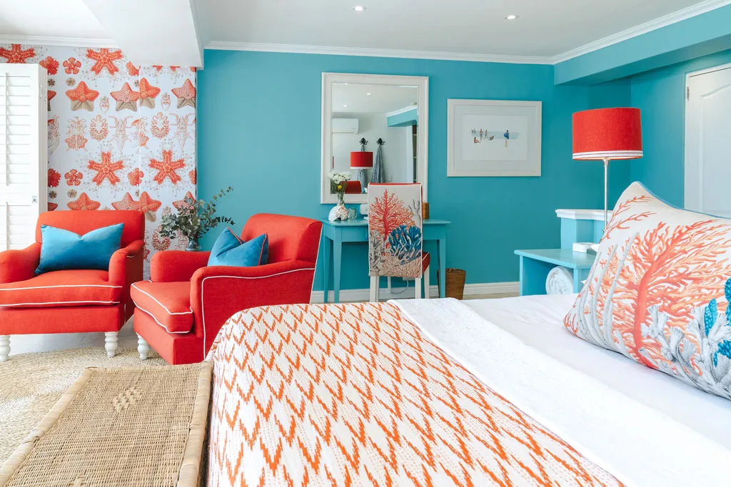 Bright bedroom with coral and turquoise decor red armchairs and patterned wallpaper