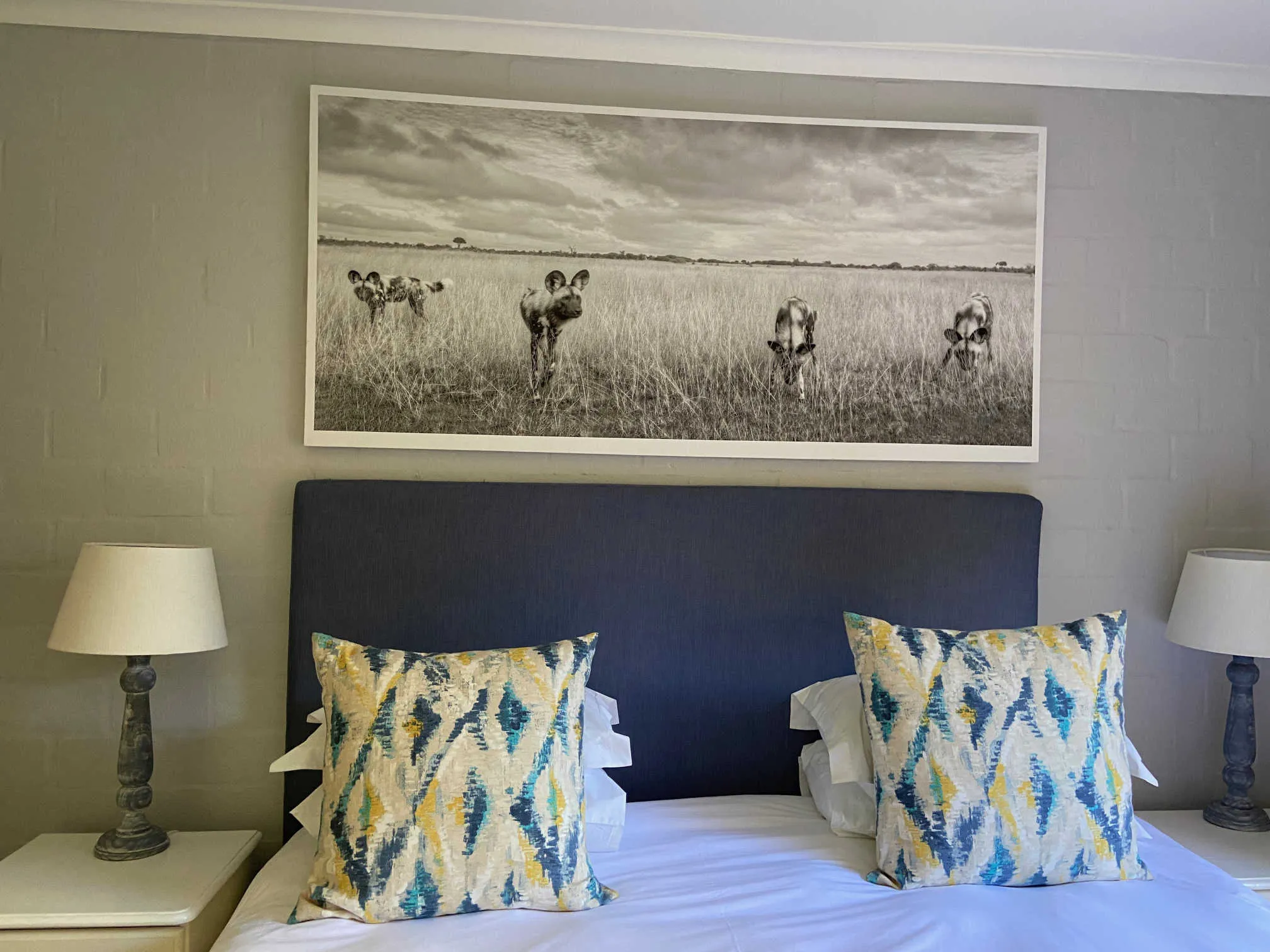 Bedroom with large nature photo above bed two patterned pillows and bedside lamps