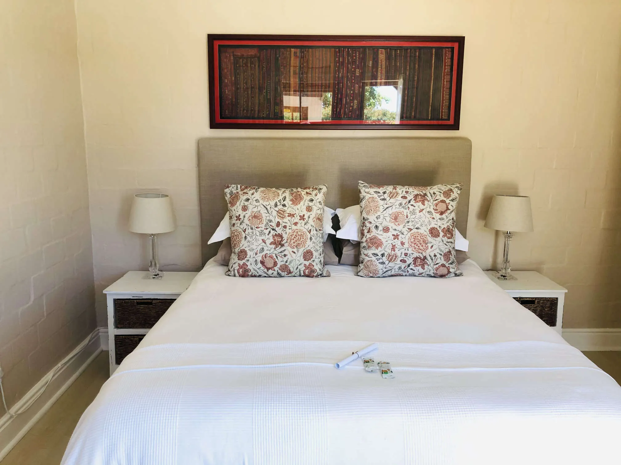 Neatly made bed with floral pillows and bedside lamps in a simple bedroom