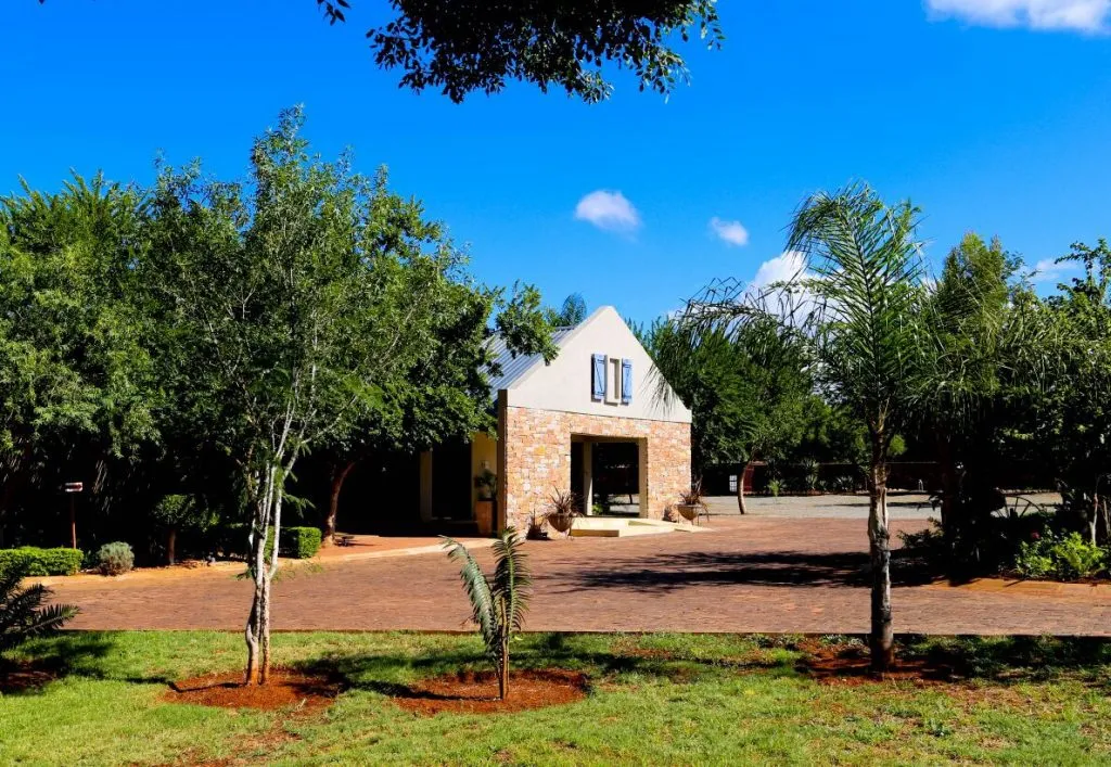 A brick building with trees and a paved path in a sunny garden