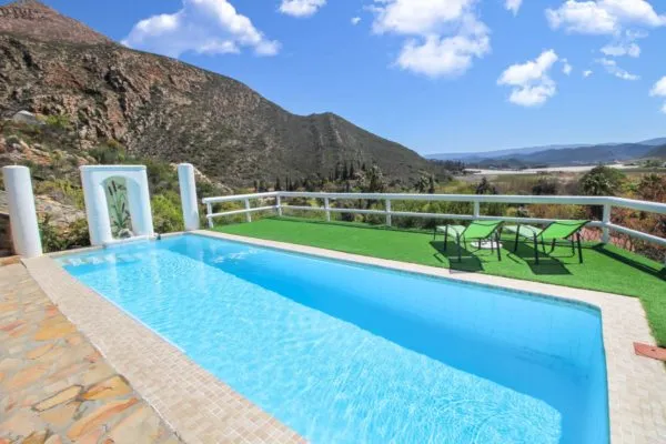Swimming pool with green lounge chairs and mountainous landscape in the background