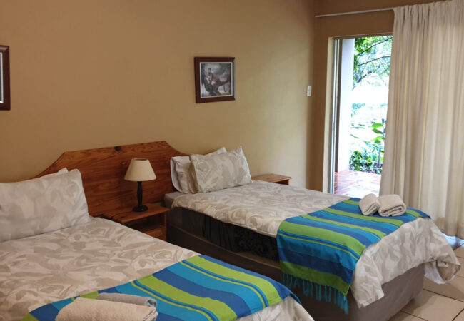 Two single beds with colorful blankets in a tidy bedroom with open door.