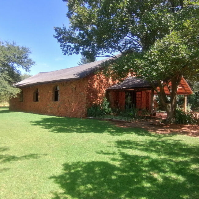 A rustic stone house with a green lawn and large tree providing shade.
