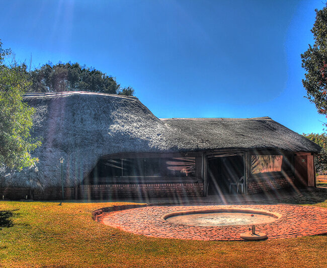 A traditional thatched-roof house with a circular brick patio in a sunny yard.