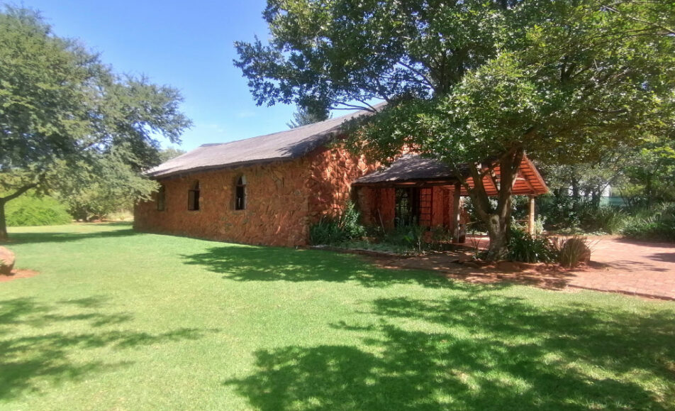 Single-story brick house with a sloped roof in a green, leafy yard.