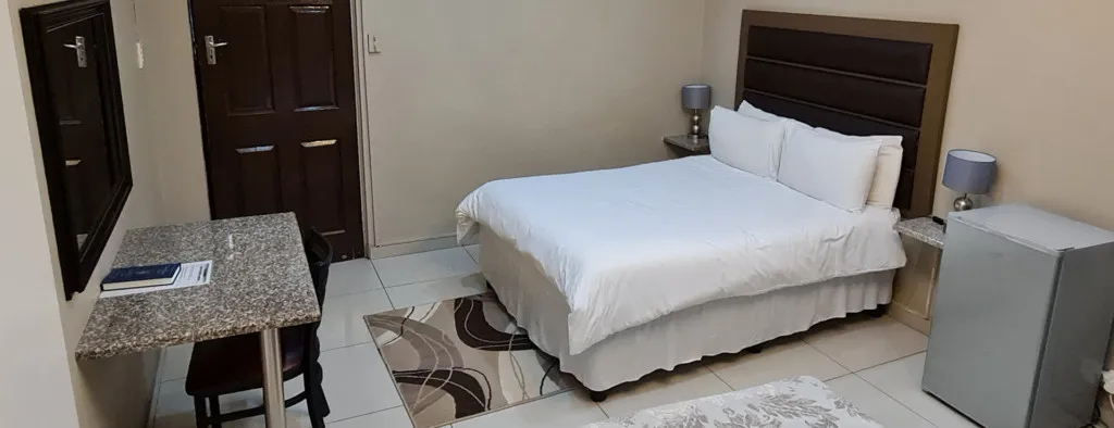 Neat bedroom with bed desk chair and small fridge tiled floor