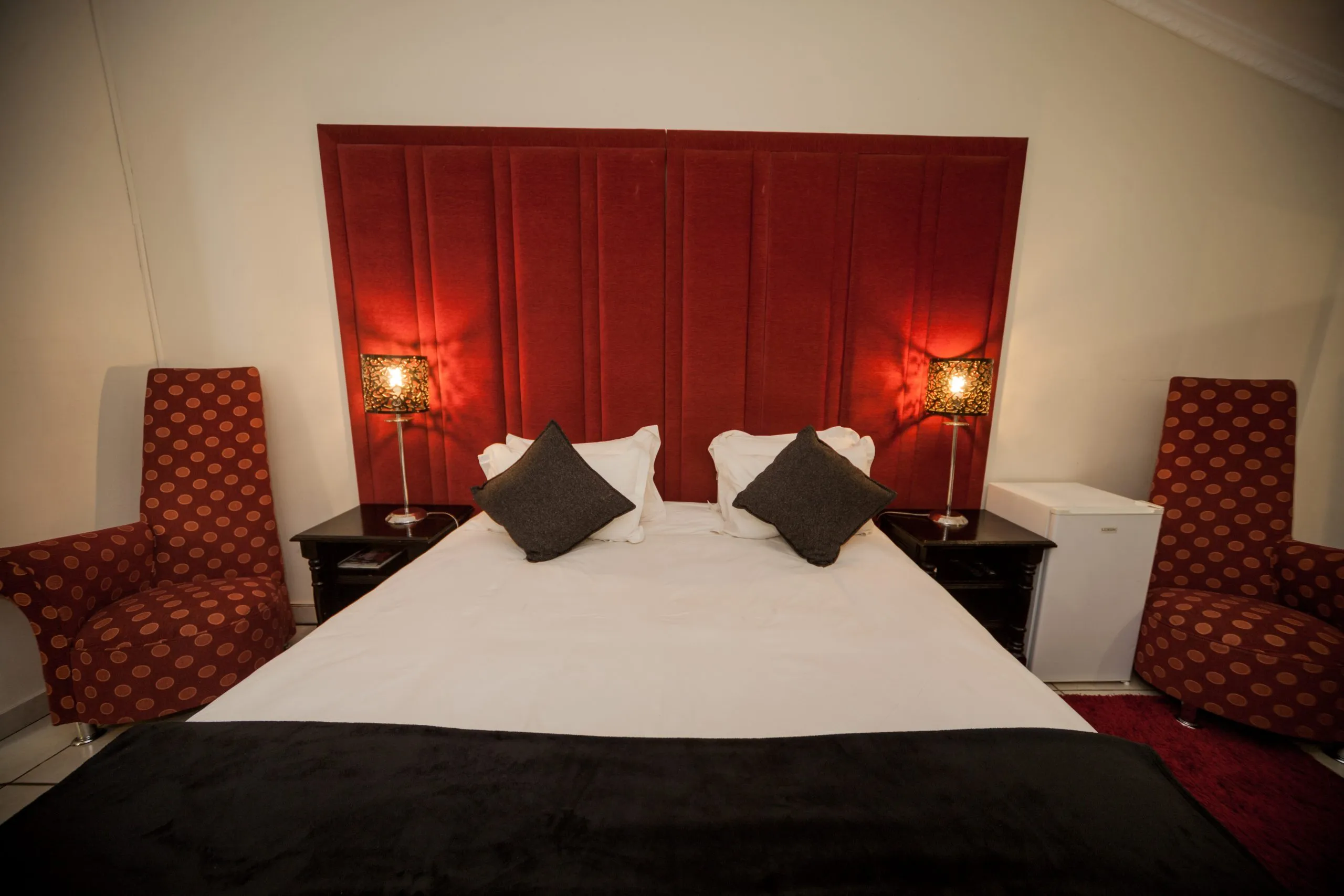 Bedroom with a large bed red headboard and matching armchairs