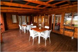 Wooden deck with white chairs and tables surrounded by wooden walls and windows