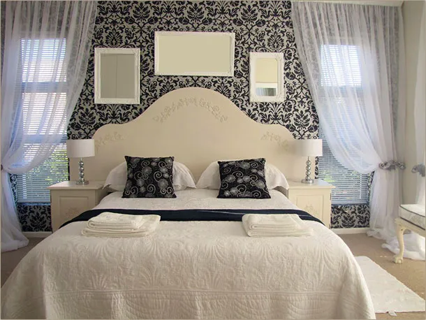 Elegant bedroom with a large bed patterned wallpaper and sheer white curtains