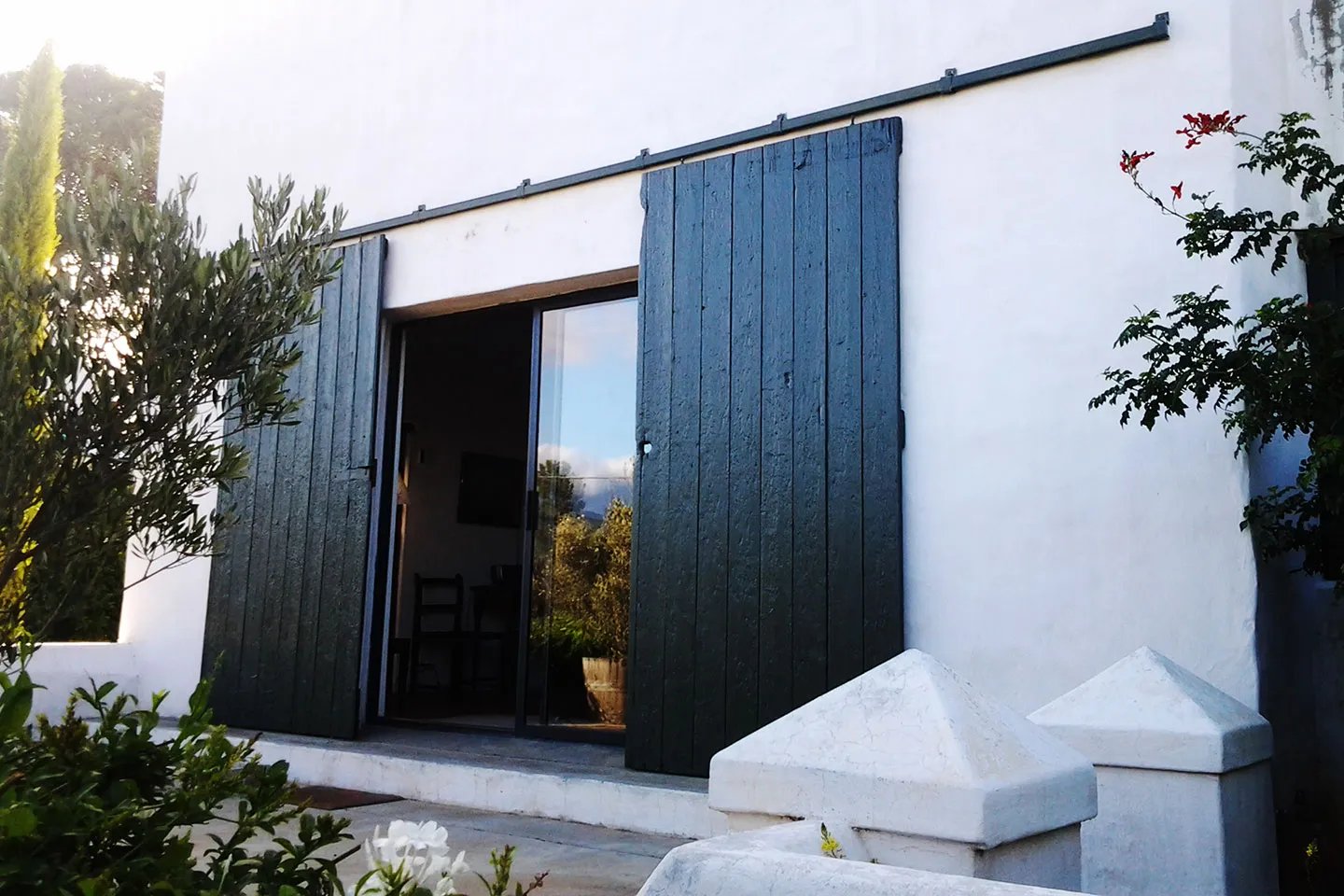 White building with dark green sliding doors and surrounding greenery