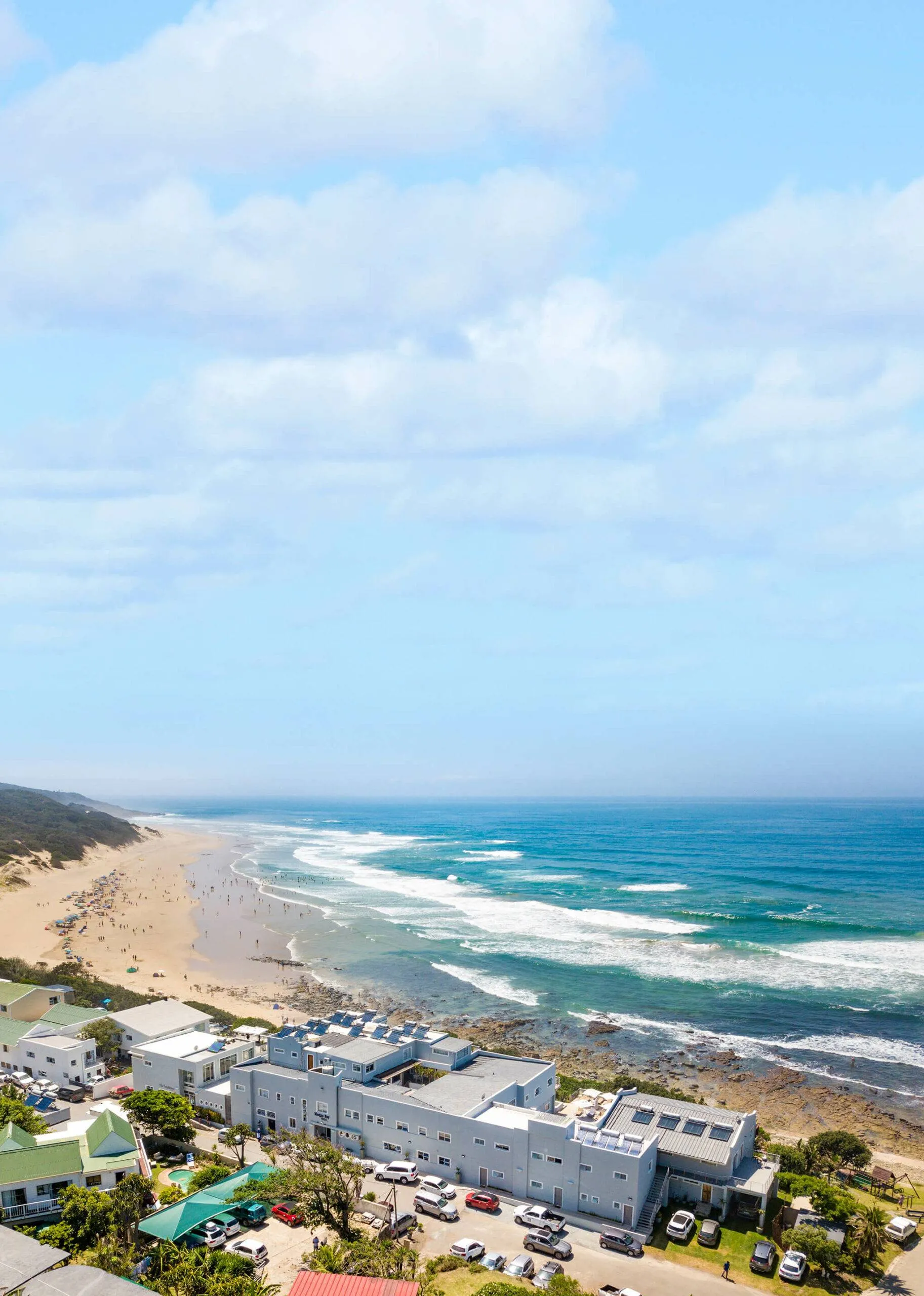 Beachfront buildings with a view of sandy shore and ocean waves under blue sky