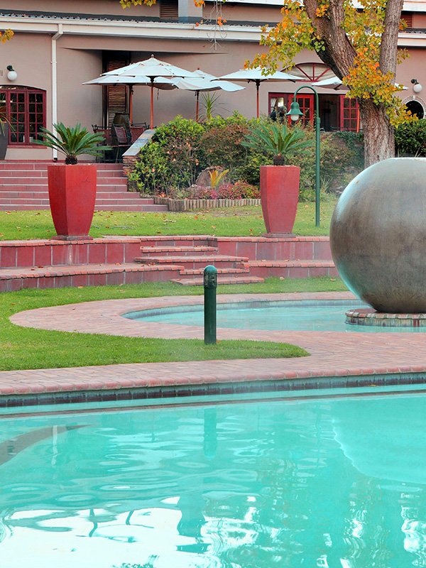 Swimming pool with large spherical sculpture and red planters in a garden setting.