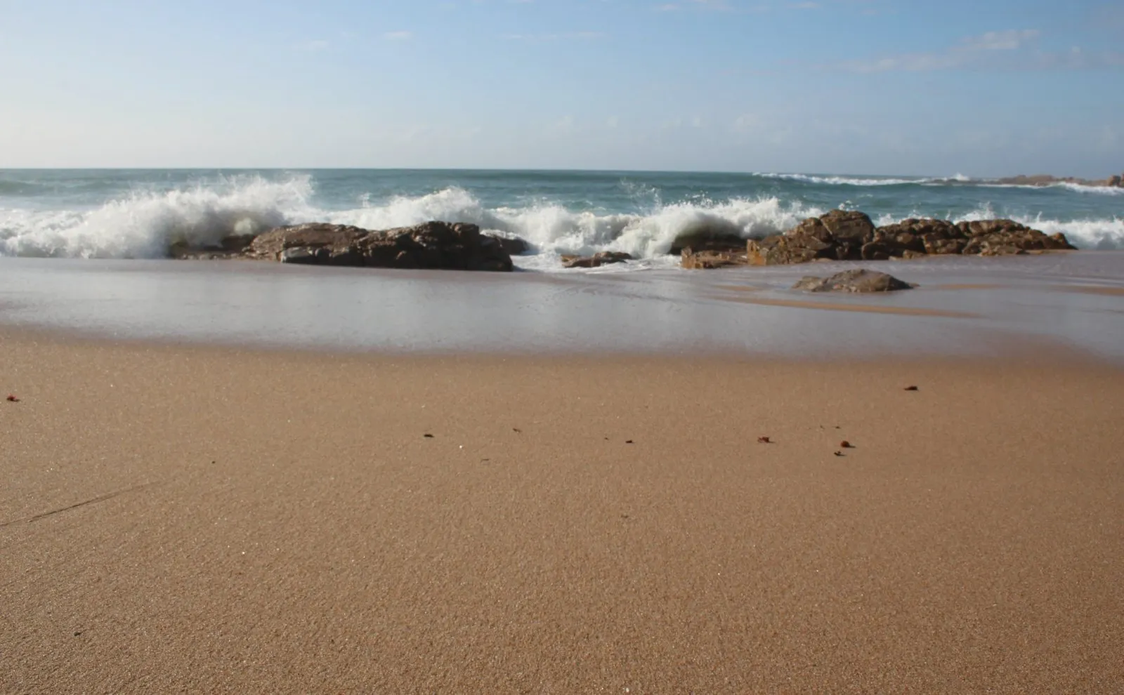 Sandy beach with waves crashing against rocks under a clear sky
