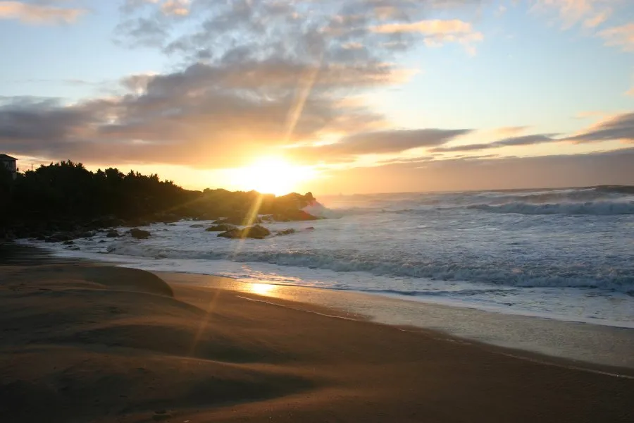 Sunset over a beach with waves crashing on rocks and sand