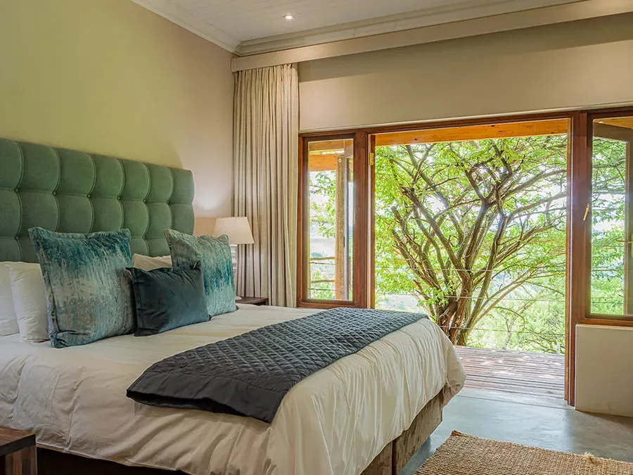 Bedroom with large bed pillows and open doors to a treefilled view