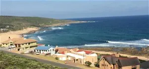 Coastal village with colorful houses overlooking a sandy beach and ocean waves