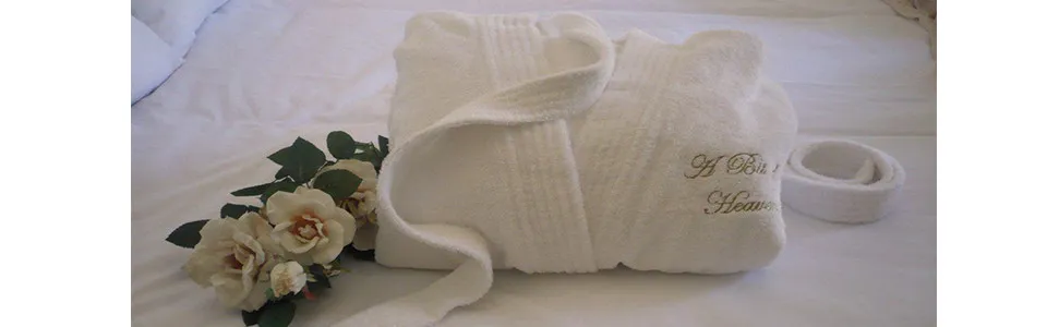 White bathrobe with embroidery on a bed with flowers beside it
